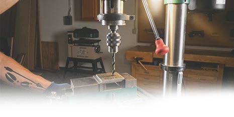 A person drilling into a block of metal using a grizzly drill press