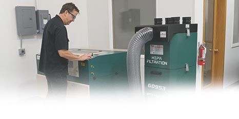 a person standing next to a cnc laser cutter that is hooked up to the grizzly G0953 hepa filtration unit