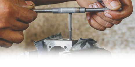 someone using a tap connected to a handle to create a threaded hole in a metal workpiece